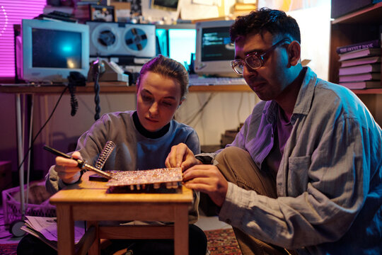 Two young people repairing old computer detail, using soldering iron, medium shot
