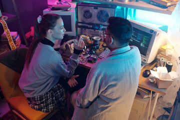 Young woman speaking with male colleague while they smoking during break, vintage computer displaying running programming code in background, high angle
