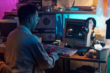 Male hacker decoding data at wooden table with retro computer displaying running code, copy space