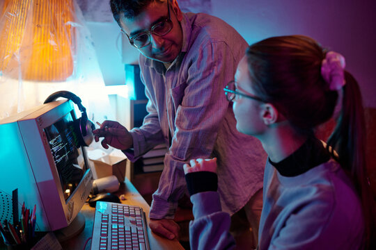 Young man with cigarette pointing at vintage computer monitor displaying programming code while discussing it with girl sitting at desk