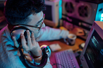 High angle view of young male hacker turning on retro tape recorder and listening to recording with headphones in room with purple and blue light
