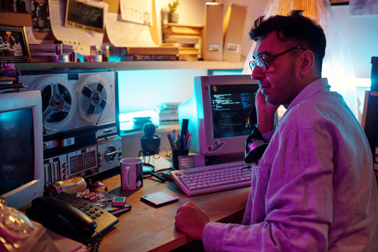 Young male hacker turning on retro tape recorder and listening to recording with headphones in cluttered room
