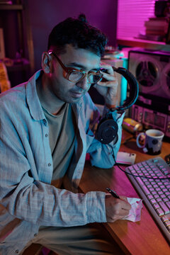 Vertical shot of male hacker with headphones writing on piece of paper when listening to old tape recording and decoding data