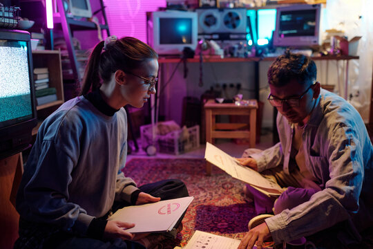 Young hackers examining white folders labeled top secret and opening them while working together sitting on floor