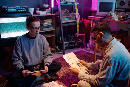 Two diverse young hackers looking through criminal profiles working on secret project when sitting on carpet with two piles of papers