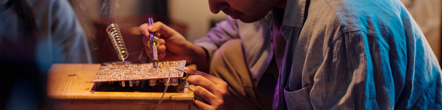Male technician soldering motherboard of vintage computer placed on wooden stool