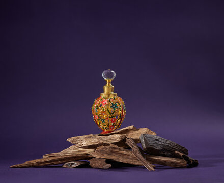A bottle of agarwood perfume with pieces of agarwood on a purple background. Full depth of field