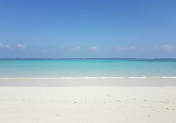 Obraz premium Tranquil turquoise waters lapping a pristine white sand beach under a vibrant blue sky, a perfect tropical paradise.
