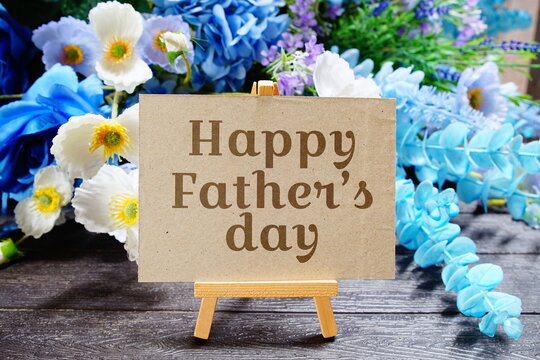 Happy father's day text write on paper card with wooden easel and flowers decoration on wooden background