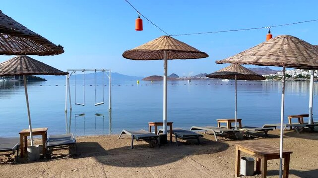 Summer vacation concept. Beautiful sandy beach with umbrellas, sun loungers and swings on the Aegean Sea
