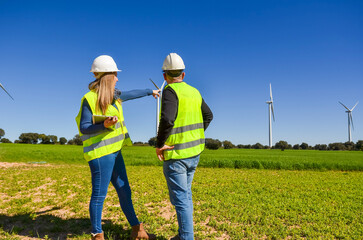 Engineers analyzing wind turbines in green field for renewable energy