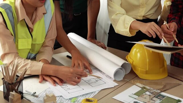 Smart architect and safety engineer discussion about building blueprint on table with architectural document, measurement tools and wooden block scatter around at modern office. Closeup. Delineation.