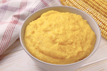 Delicious corn porridge in a bowl on a white wooden table.