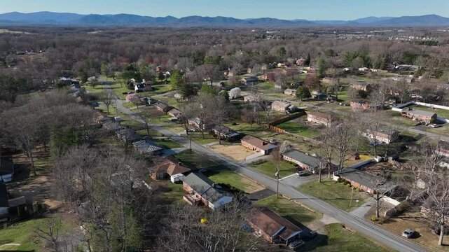 Aerial establishing shot of american suburb neighborhood with one Family houses during early spring season. Street with houses and homes and leafless trees. Mountains in background. Virginia State.