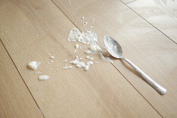 Spilled yogurt on wooden floor with spoon 