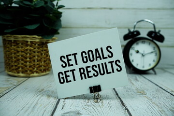 Set Goals Get Results text on paper card with alarm clock on wooden background