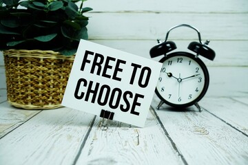 Free To Choose text on paper card with alarm clock on wooden background