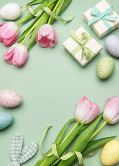 Easter eggs, tulips and gift boxes forming a frame on light green background