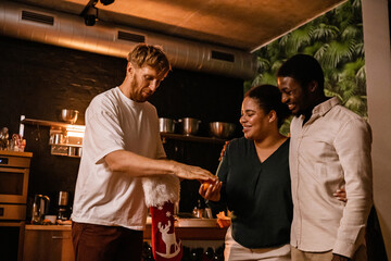 A cute Black couple in their late 30s, standing in the living room of a cozy home and smiling widely, as their mid-40s White male friend gifts them a tangerine from a Christmas stocking