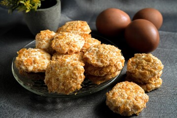 A plate filled with golden cornflake cookies alongside brown eggs on a textured surface, creating a rustic and inviting atmosphere suitable for baking, desserts, and culinary themes.