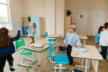 A young, school-aged White boy with blond hair, who is dressed in a button-up shirt, standing next...