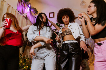 A group of four multiethnic young adult women dressed in stylish clothes dancing together in a room...