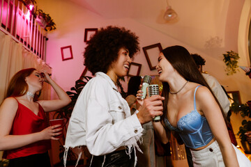 A young Latina woman in her late 20s, dancing and singing into wireless microphones together with...