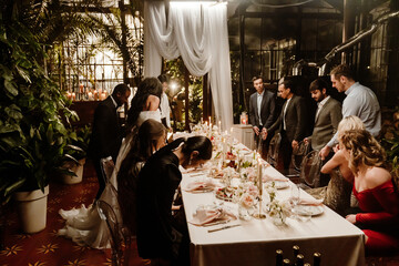 A large, diverse group of wedding guests, who are all dressed in fine clothing, sitting down at the...