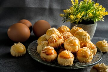 Freshly baked cheese-topped Nastars arranged on a plate, paired with eggs and a decorative plant in a cozy setting, showcasing homemade treats perfect for food and culinary presentations.