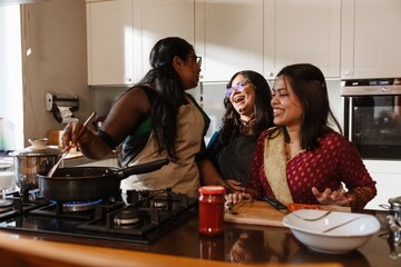 Three smiling Indian women in their early 30s wearing traditional clothes are laughing, and...