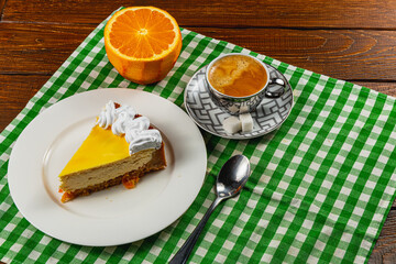Cheesecake slice with coffee and orange on a checkered tablecloth
