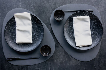 Modern minimalist table setting with plates, napkins, chopsticks, and dark tones
