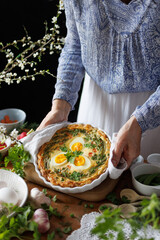 Woman holding casserole dish with quiche with boiled eggs and vegetables, close-up. Easter food...