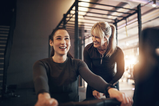Smiling female instructor offering encouragement to a fit young woman working out on a rowing machine during a gym exercise class - Powered by Adobe