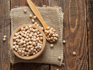 Close-up of a bowl filled with raw chickpeas surrounded by scattered legumes and a wooden spoon