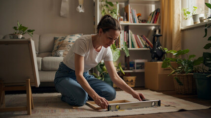 Woman measuring frame on the floor while preparing to decorate her living room in a cozy and bright apartment