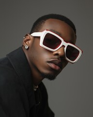 Fototapeta premium Stylish young man poses confidently with trendy sunglasses in a modern studio setting