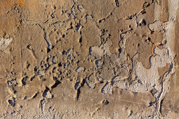 Beige-colored section of a weathered house facade with traces of time. Peeling wall paint and crumbling plaster on a run-down house (Germany). Structures are emphasized by sun fro from the side.