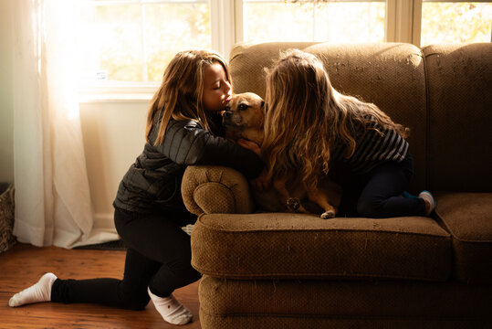 Sisters kissing puggle dog on couch