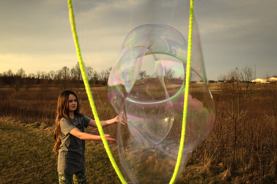 Tween girl popping giant bubble in sunny field