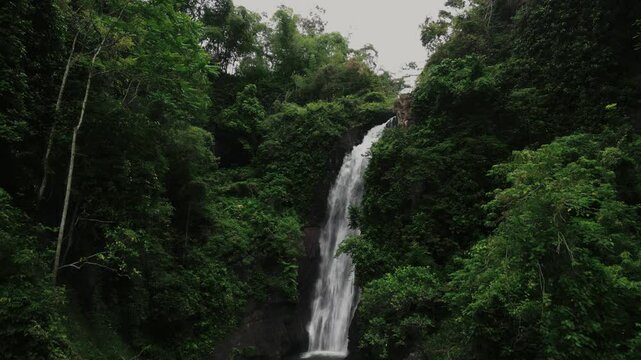 Aerial drone shot of Hidden waterfall in tropical forest java indonesia, drone flying towards the waterfall and slowly tilting down the camera, revealing some huge rocks.