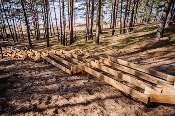 Wooden stair stringers under construction on a sandy hillside in a pine forest, supported by metal...