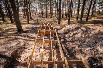 Wooden stairway framework under construction on a sandy forest hill, surrounded by trees and...