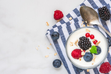 Greek yogurt with fresh berries, oats and mint in a glass on napkin over white background with...