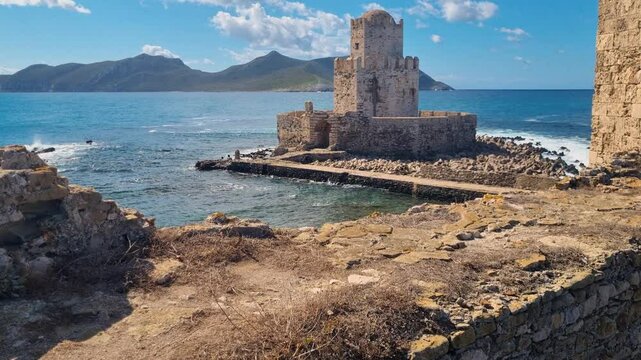A revealing shot of the tower of the Venetian fortress in Methoni, Greece, standing against the deep blue Mediterranean Sea beneath a clear blue sky