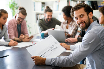 Diverse group of happy employees analyzing reports with digital device, working together in office