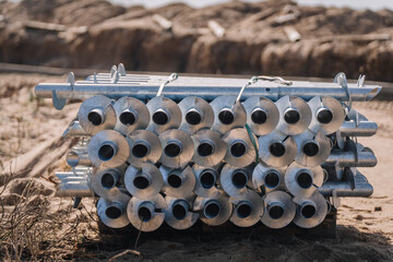 Close-up view of a stacked bundle of large metal ground screws placed on a pallet at a sandy...