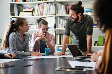 Diverse group of happy employees analyzing reports with digital device, working together in office