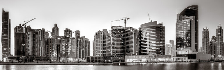 Monochrome city skyline with tall skyscrapers reflecting on calm water under a cloudy sky, Dubai Marina bay UAE