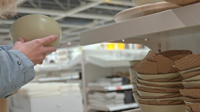 Woman customer choosing ceramic bowl in kitchenware section of store. Concept of home shopping and interior lifestyle